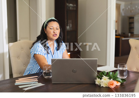 Hispanic woman working on silver-gray laptop at dining table with pastel swatches and water glasses 133836195