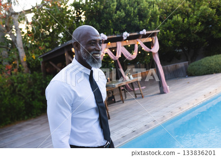 African American senior man standing on wooden deck beside pool under decorated pergola, copy space African American senior man standing on wooden deck beside pool under decorated pergola, copy space 133836201