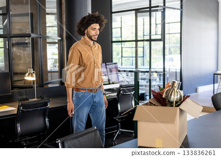 Man standing at workstation in open-plan office unpacking box with lamp and plant, copy space 133836261