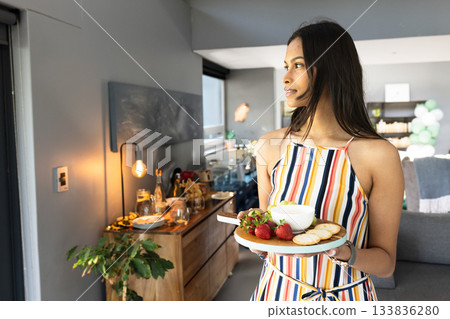 Asian woman holding platter with dip, crackers and strawberries in open kitchen, copy space 133836280