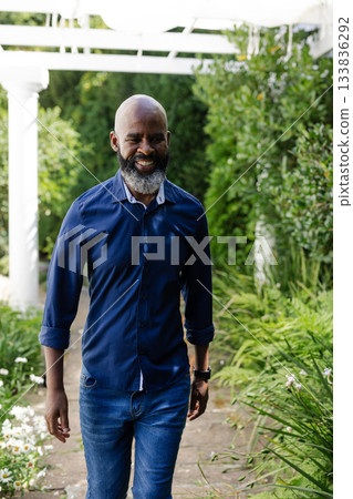 Mature African American man walking stone path with daisies and shrubs under pergola wearing watch Mature African American man walking stone path with daisies and shrubs under pergola wearing watch 133836292
