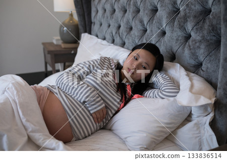 Pregnant Asian woman lying on king-size bed at home with tufted headboard, lamp and books Pregnant Asian woman lying on king-size bed at home with tufted headboard, lamp and books 133836514