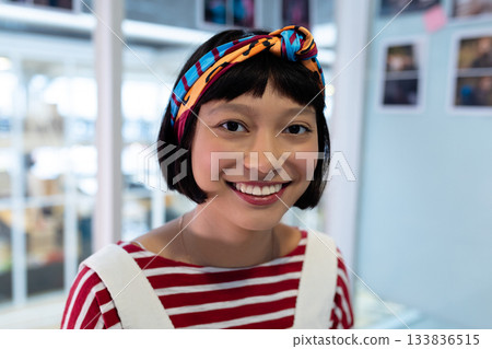 Adult Asian woman smiling wearing headband, striped shirt, necklace in studio with glass panels Adult Asian woman smiling wearing headband, striped shirt, necklace in studio with glass panels 133836515