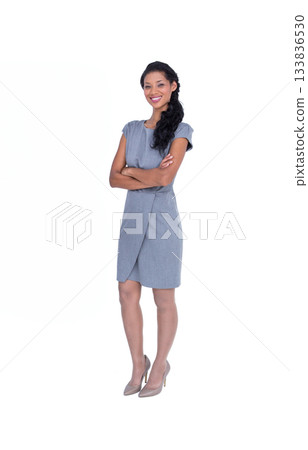 Woman posing against white studio backdrop wearing grey sheath dress and neutral high-heeled pumps 133836530