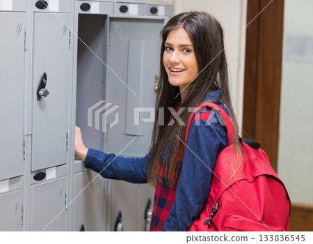 Teenage female student opening light gray locker in school corridor with red backpack, copy space Teenage female student opening light gray locker in school corridor with red backpack, copy space 133836545