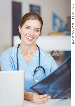 Female doctor examining radiograph film at clinic office workspace with laptop and stethoscope 133836547