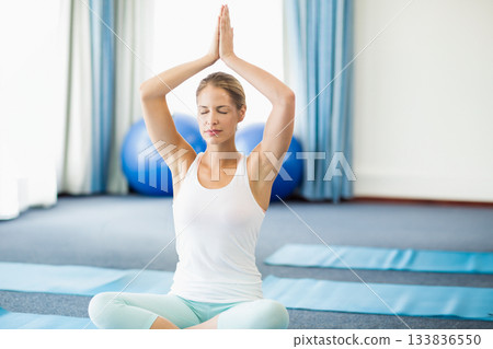 Woman practicing lotus pose on yoga mat in fitness studio with blue exercise balls Woman practicing lotus pose on yoga mat in fitness studio with blue exercise balls 133836550