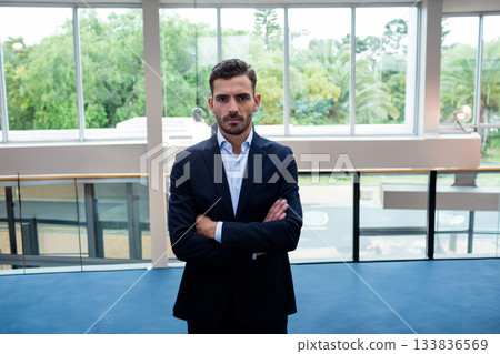 Male business professional standing in modern lobby near glass railing and floor-to-ceiling windows Male business professional standing in modern lobby near glass railing and floor-to-ceiling windows 133836569