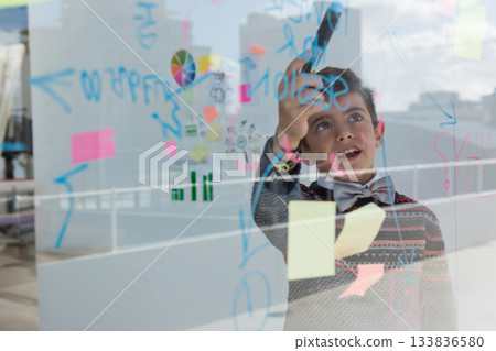 School-age boy standing behind glass panel sketching diagrams with marker at office, copy space 133836580