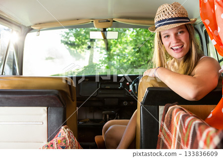 Woman leaning over driver seat in campervan wearing straw hat and polka dot blouse, copy space 133836609
