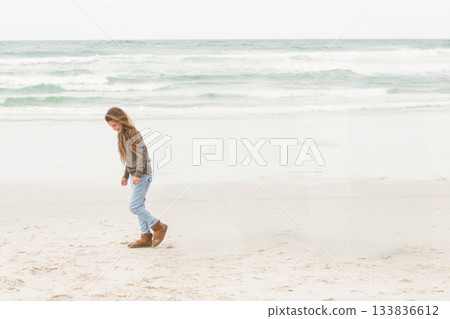 Child girl walking on sandy beach leaving footprints in wet sand near calm waves, copy space 133836612