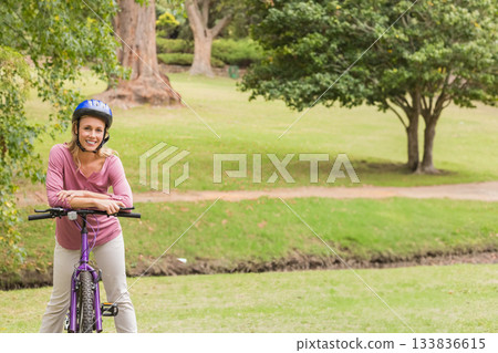 Woman leaning on purple bicycle handlebars in park wearing blue helmet, copy space Woman leaning on purple bicycle handlebars in park wearing blue helmet, copy space 133836615