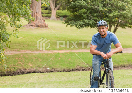 Man leaning on black bicycle wearing multi-color helmet near dirt walking path in park, copy space Man leaning on black bicycle wearing multi-color helmet near dirt walking path in park, copy space 133836618