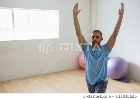 30s man performing lunge pose on wooden floor in exercise room with stability balls, copy space 133836620