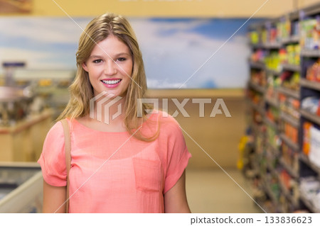 Woman carrying shoulder bag and smiling inside supermarket aisle by refrigerated display unit Woman carrying shoulder bag and smiling inside supermarket aisle by refrigerated display unit 133836623