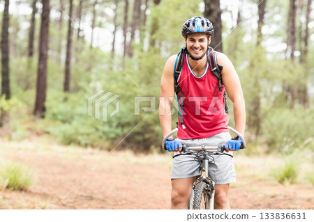 Man riding bicycle through pine forest wearing helmet, red tank top, blue gloves, carrying backpack Man riding bicycle through pine forest wearing helmet, red tank top, blue gloves, carrying backpack 133836631