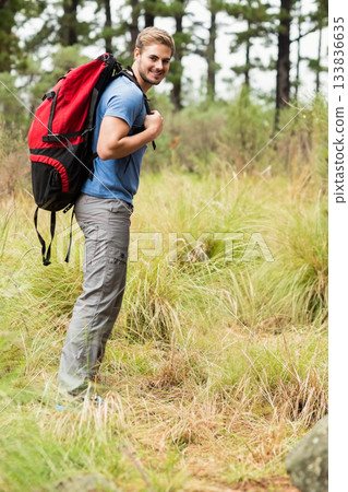 Male hiker smiling in pine forest clearing wearing hiking shoes and carrying red and black backpack Male hiker smiling in pine forest clearing wearing hiking shoes and carrying red and black backpack 133836635