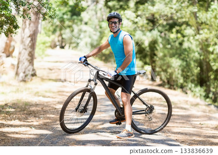 Man posing on mountain bike at forest trail wearing cycling jersey, helmet, sunglasses and gloves Man posing on mountain bike at forest trail wearing cycling jersey, helmet, sunglasses and gloves 133836639