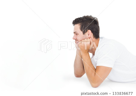 Man lying on smooth white studio surface on elbows facing left in minimalist portrait, copy space 133836677
