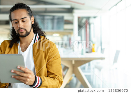 Man sitting at coworking space wearing bomber jacket holding tablet near bright windows, copy space Man sitting at coworking space wearing bomber jacket holding tablet near bright windows, copy space 133836970