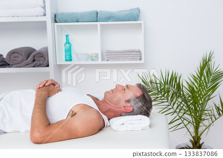 Male client in 50s relaxing on massage table in spa with rolled towel and potted palm Male client in 50s relaxing on massage table in spa with rolled towel and potted palm 133837086