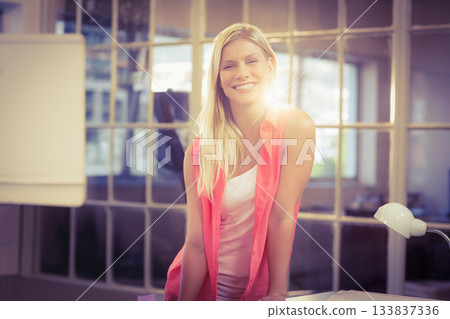 Smiling woman leaning forward on desk at office with flip chart, desk lamp and glass partition Smiling woman leaning forward on desk at office with flip chart, desk lamp and glass partition 133837336