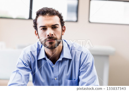 Man sitting on chair in modern office wearing light blue dress shirt near large windows Man sitting on chair in modern office wearing light blue dress shirt near large windows 133837343