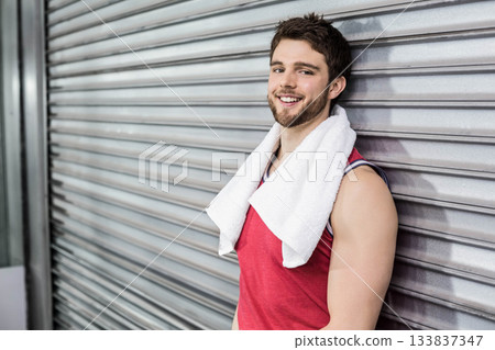 Man leaning back against shutter inside gym wearing red sleeveless top and white towel, copy space 133837347