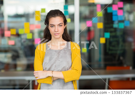 Woman wearing yellow cardigan crossing arms at office in front of partition with sticky notes Woman wearing yellow cardigan crossing arms at office in front of partition with sticky notes 133837367