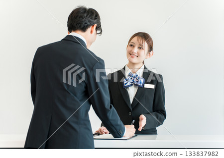 一名男子正在辦理入住手續、在櫃檯簽名，一名女酒店員工正在為他服務。 133837982