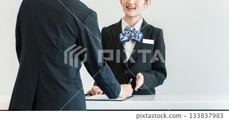 一名男子正在辦理入住手續、在櫃檯簽名，一名女酒店員工正在為他服務。 133837983