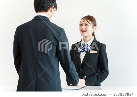 一名男子正在辦理入住手續、在櫃檯簽名，一名女酒店員工正在為他服務。 133837984