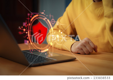 Person using laptop computer with glowing red security shield hologram, symbolizing cybersecurity, data protection, privacy, firewall, encryption, and online safety. 133838533