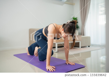 Young woman practicing yoga indoors on a purple mat, showcasing strength and flexibility in a modern living space with natural light and serene atmosphere Young woman practicing yoga indoors on a purple mat, showcasing strength and flexibility in a modern living space with natural light and serene atmosphere 133839642