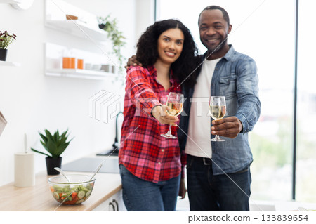 A smiling couple in a kitchen clink glasses of wine, celebrating a special occasion or enjoying a meal together. A smiling couple in a kitchen clink glasses of wine, celebrating a special occasion or enjoying a meal together. 133839654