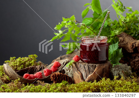 A jar of raspberry jam with fresh berries on an old tree trunk in the forest. A jar of raspberry jam with fresh berries on an old tree trunk in the forest. 133840297