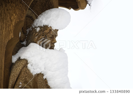 Wooden sculpture of Jesus Christ covered in snow against a bright sky 133840890
