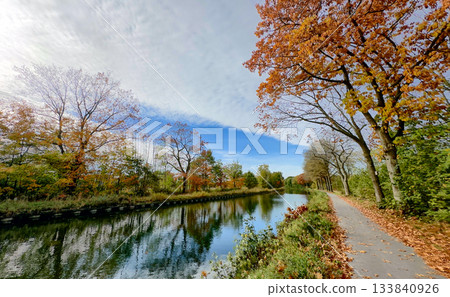 Crisp air and amber leaves beside calm reflective water 133840926