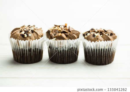 Chocolate cupcakes are showing in flat design on white table with liners, frosting and toppings Chocolate cupcakes are showing in flat design on white table with liners, frosting and toppings 133841262