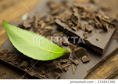 Flat design close-up is showing broken dark chocolate pieces with fresh green leaf on rustic board 133841366