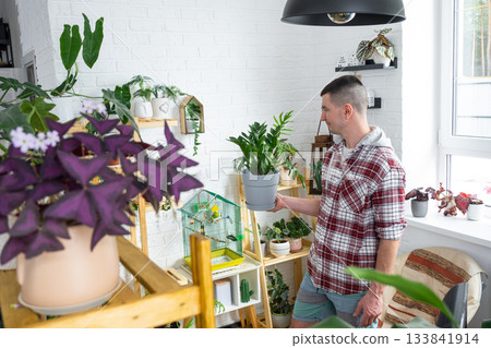 A man takes care of home-made potted plants on the shelves, waters from a watering can, his business A man takes care of home-made potted plants on the shelves, waters from a watering can, his business 133841914