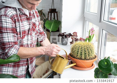A man takes care of home-made potted plants on the shelves, waters from a watering can, his business 133841917
