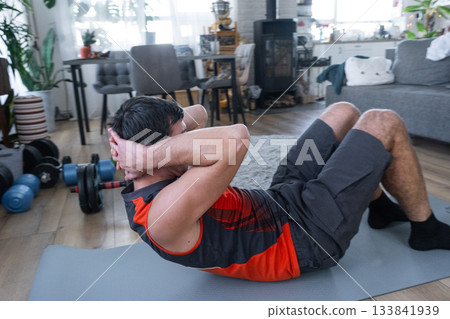 A man does abs exercises at home on a fitness carpet A man does abs exercises at home on a fitness carpet 133841939