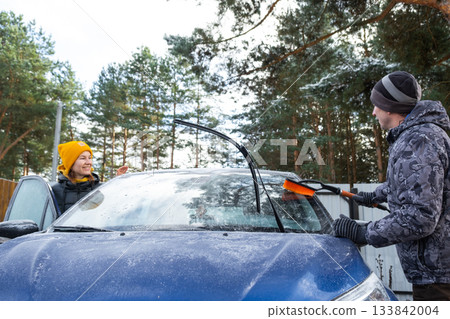 Husband and wife clean the car of ice from near the house in the yard in the autumn frosts Husband and wife clean the car of ice from near the house in the yard in the autumn frosts 133842004