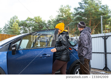 The woman gets behind the wheel, Husband and wife get into the car near the house in the yard 133842009