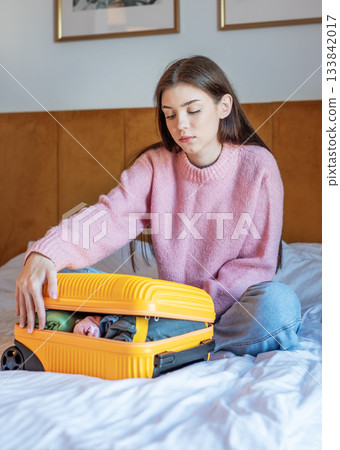 Woman packing yellow suitcase on bed for travel 133842017