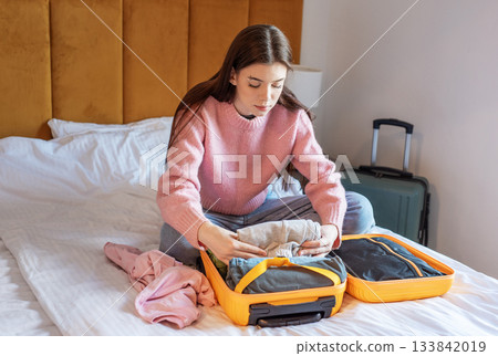 Woman packing suitcase on bed in hotel room Woman packing suitcase on bed in hotel room 133842019