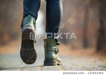 A person wearing green boots and black pants is walking on a road 133842464