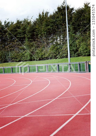 Curved red track is winding in flat design with white lanes, railing, hedge and light pole 133845574