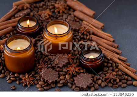 Soy scented candle in jar. Coffee beans anise, cinnamon spices. Christmas mood candles light burning background. Chocolate candy 133846220